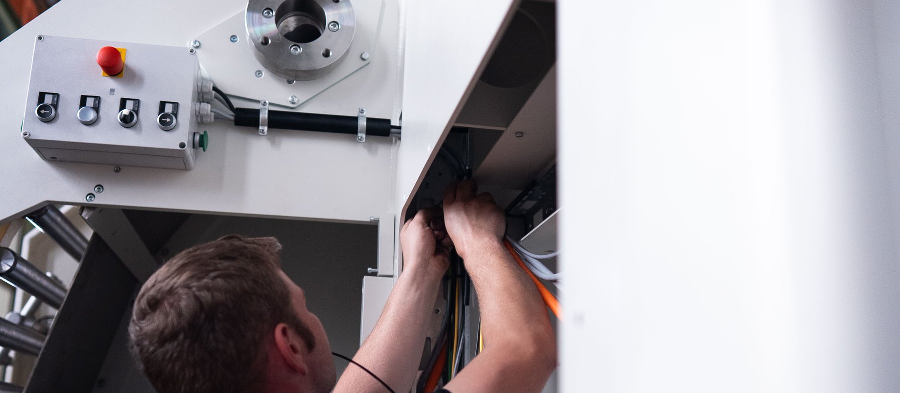 Monteur verkabelt eine weiße Industriemaschine, Not-Aus-Schalter im Bild